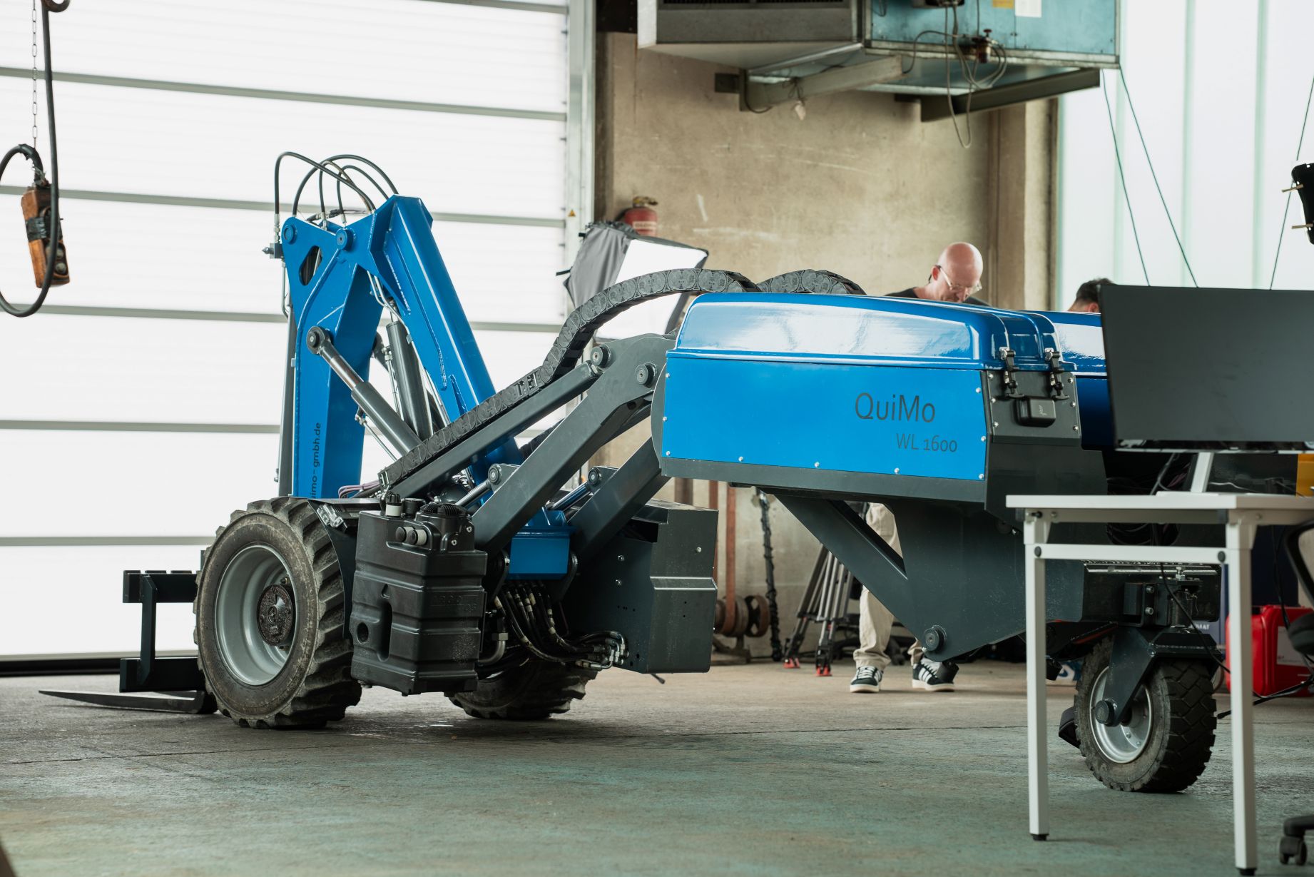 QuiMo WL1600 elektrischer Radlader beim Entladen von Material in einer Industriehalle – wendiger Kompaktlader für Bau, Industrie und Lagerlogistik.